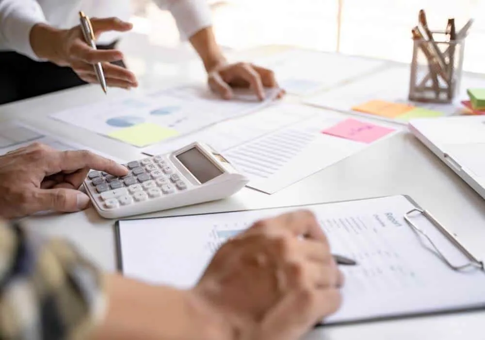 Two colleagues reviewing charts and financial documents with a calculator